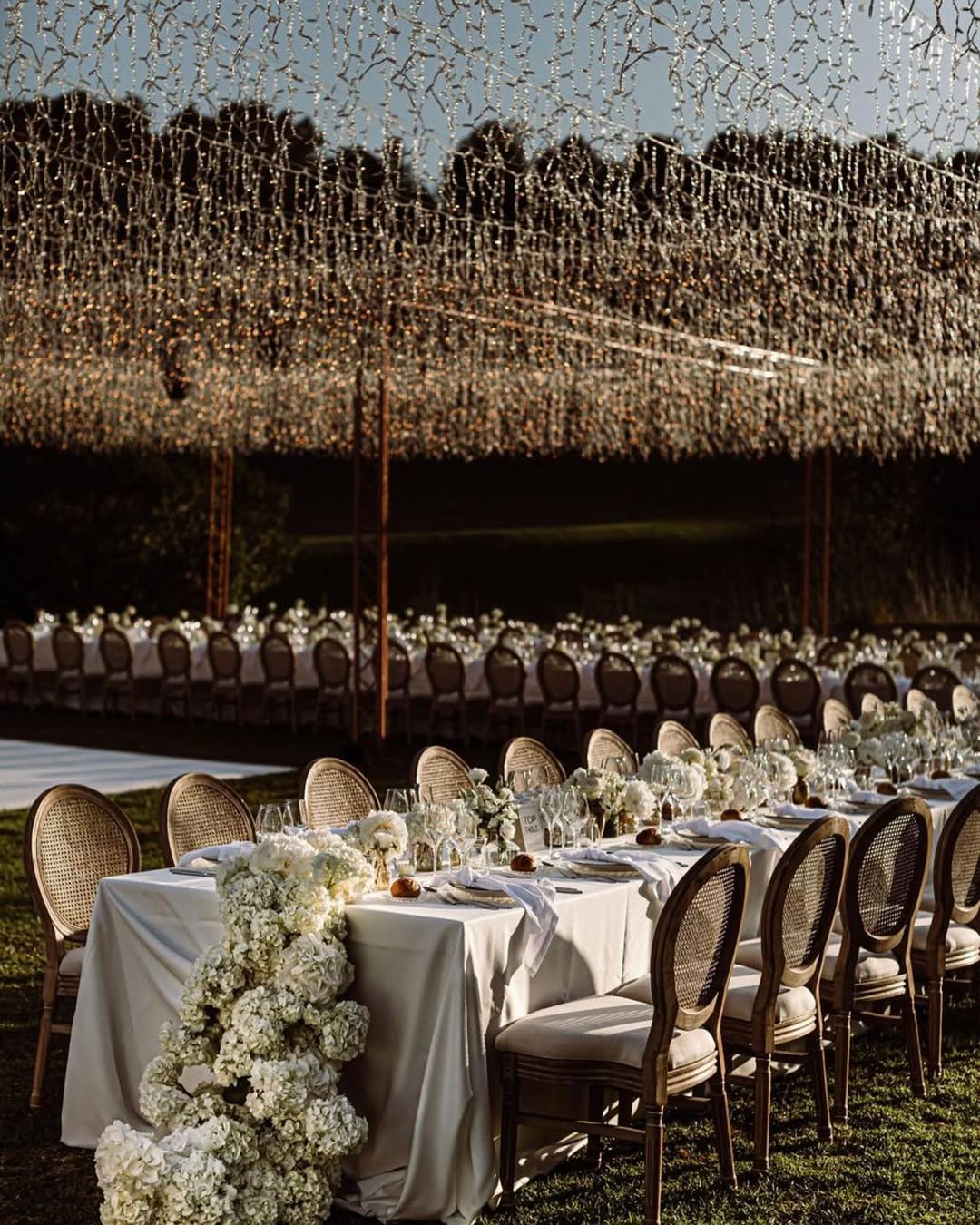 Elegant garden wedding reception with cascading fairy lights and white floral table decor at Biniorella Mallorca.