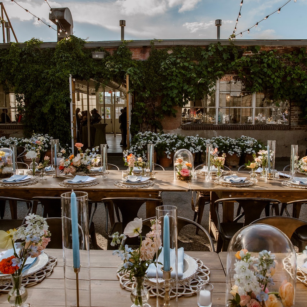 Charming outdoor reception setup at Blanc Denver with vine-covered brick walls, string lights, and colorful floral centerpieces β a trendy choice for urban Denver wedding venues.