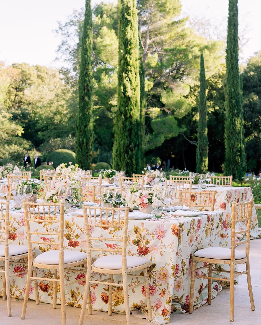 Elegant garden wedding setup at Château d’Estoublon featuring floral tablecloths and natural wood chairs, showcasing the refined beauty of a Provence France wedding.