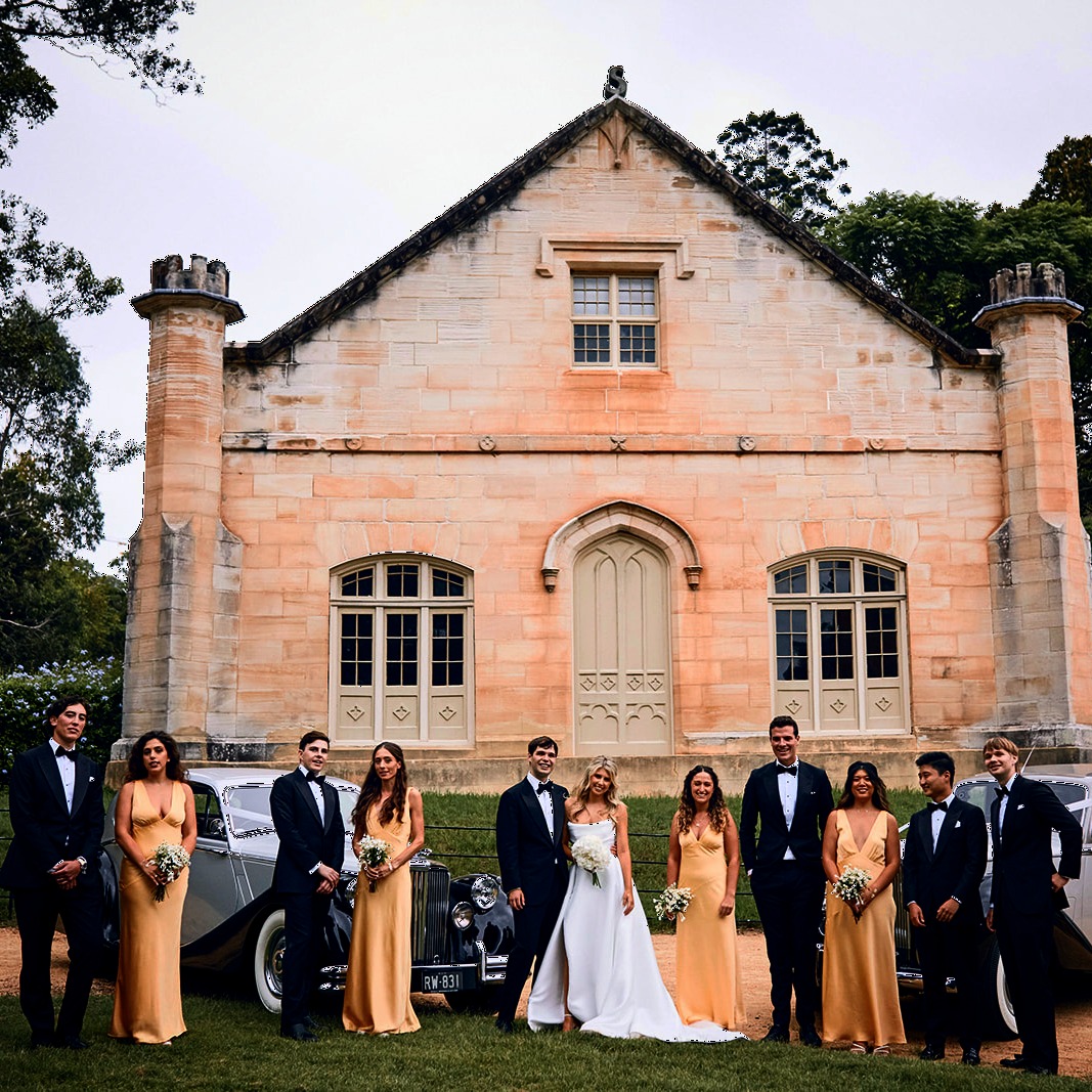A bride and groom pose with their wedding party in front of the historic sandstone faรงade of Estate Vaucluse House, showcasing the charm and timeless elegance of one of the top sydney wedding venues with colonial architecture.