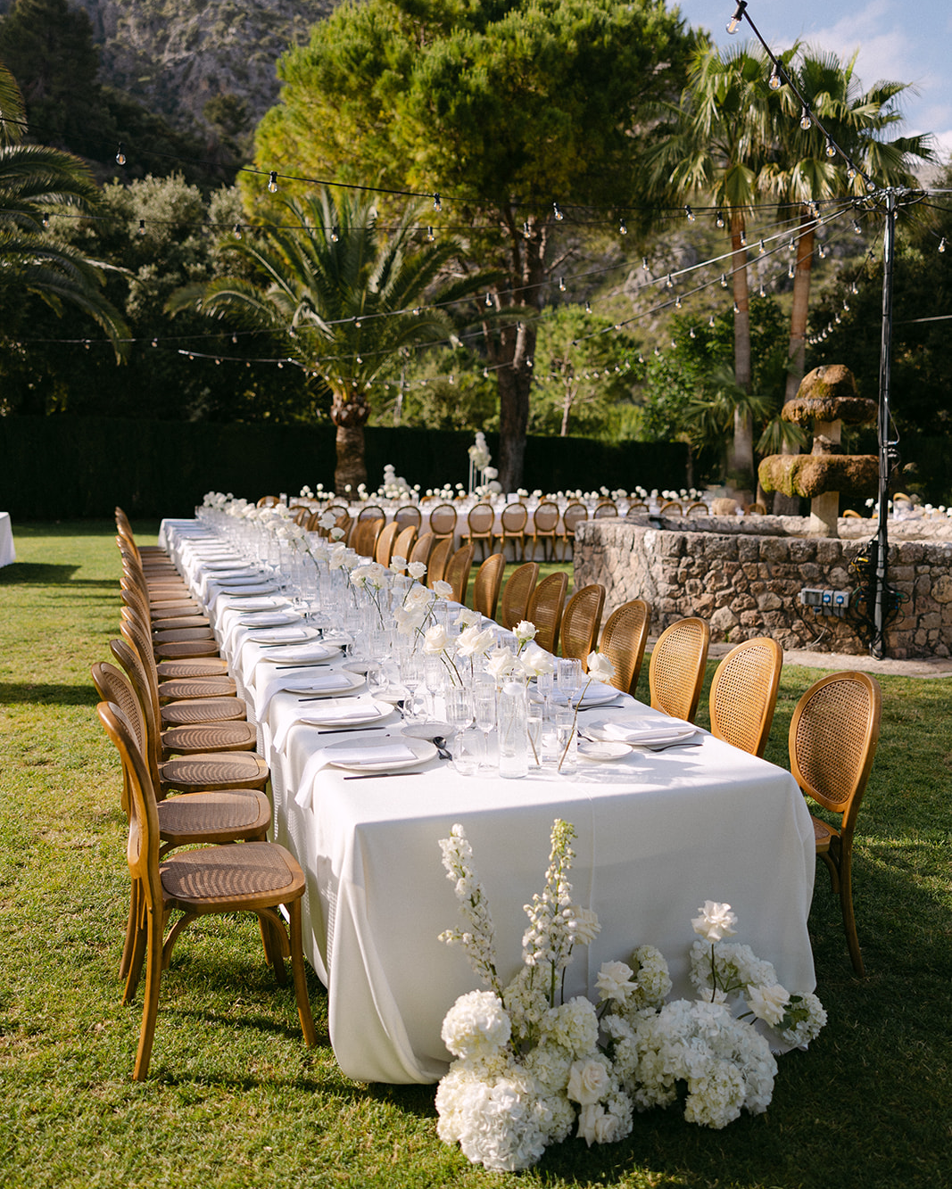 Chic outdoor wedding dinner setup beside a stone fountain under fairy lights at Finca Comassema Mallorca.