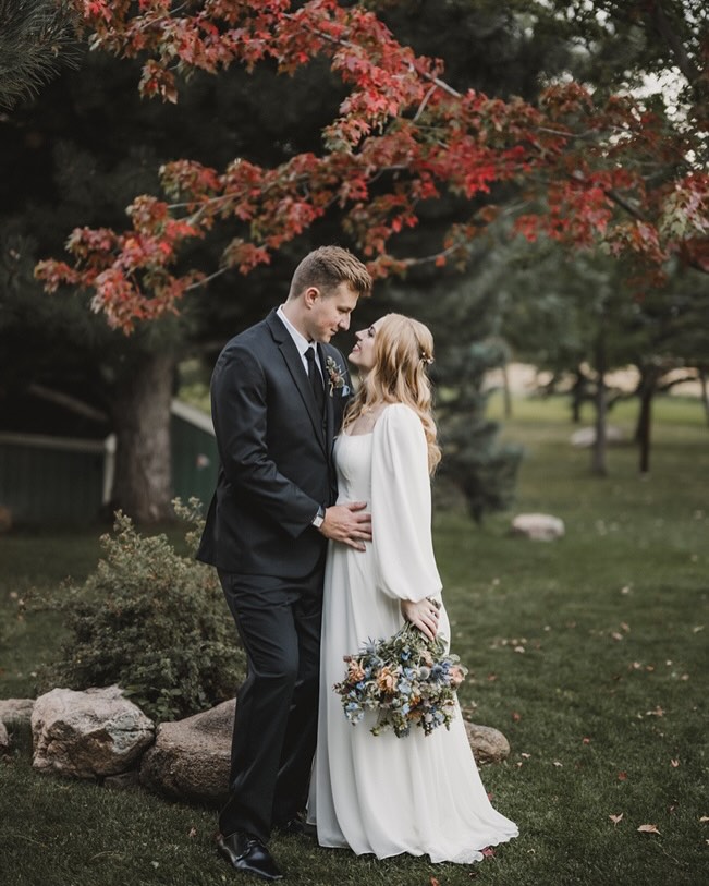 A bride and groom pose under fall foliage at The Greenbriar Inn, surrounded by vibrant autumn leaves and lush gardens β an enchanting countryside escape for Denver wedding venues.