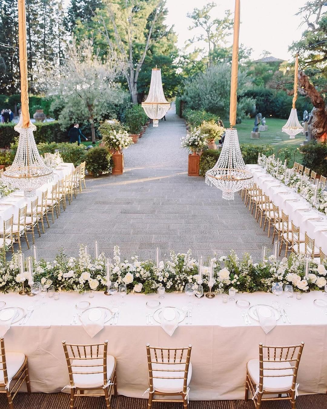 Drone shot of a dreamy wedding celebration at Villa Mangiacane, one of the most picturesque Tuscany wedding venues, surrounded by olive groves and a Renaissance estate, with guests dining on long tables in a garden at golden hour.