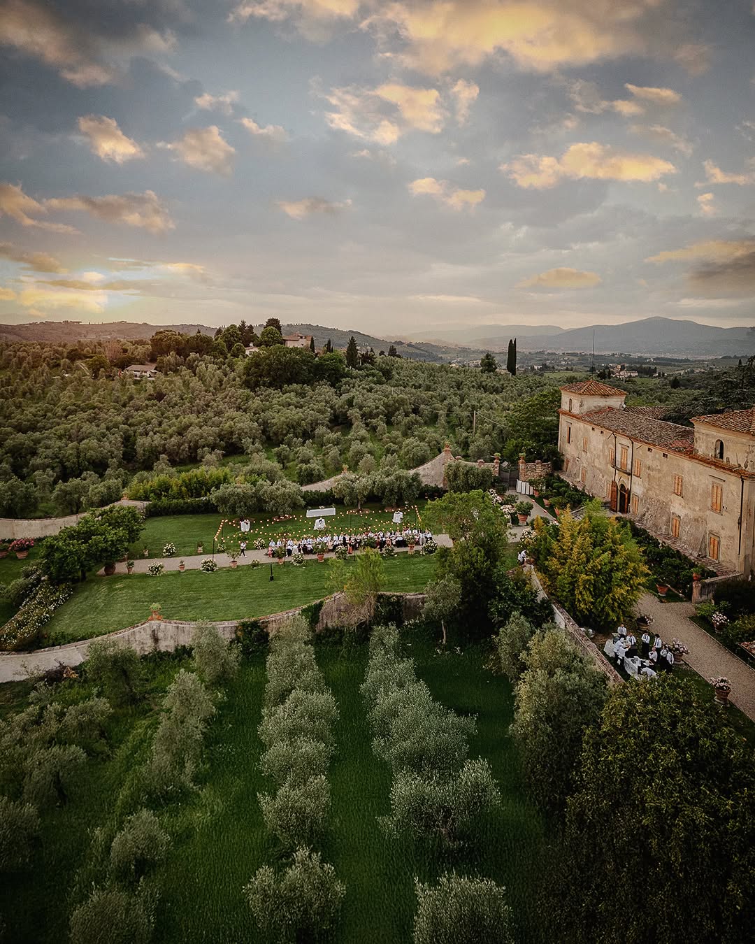 Elegant open-air reception at Villa Medicea di Lilliano, a historic Tuscany wedding venue, featuring cascading floral runners, gold Chiavari chairs, and suspended chandeliers against the backdrop of a romantic Tuscan courtyard.