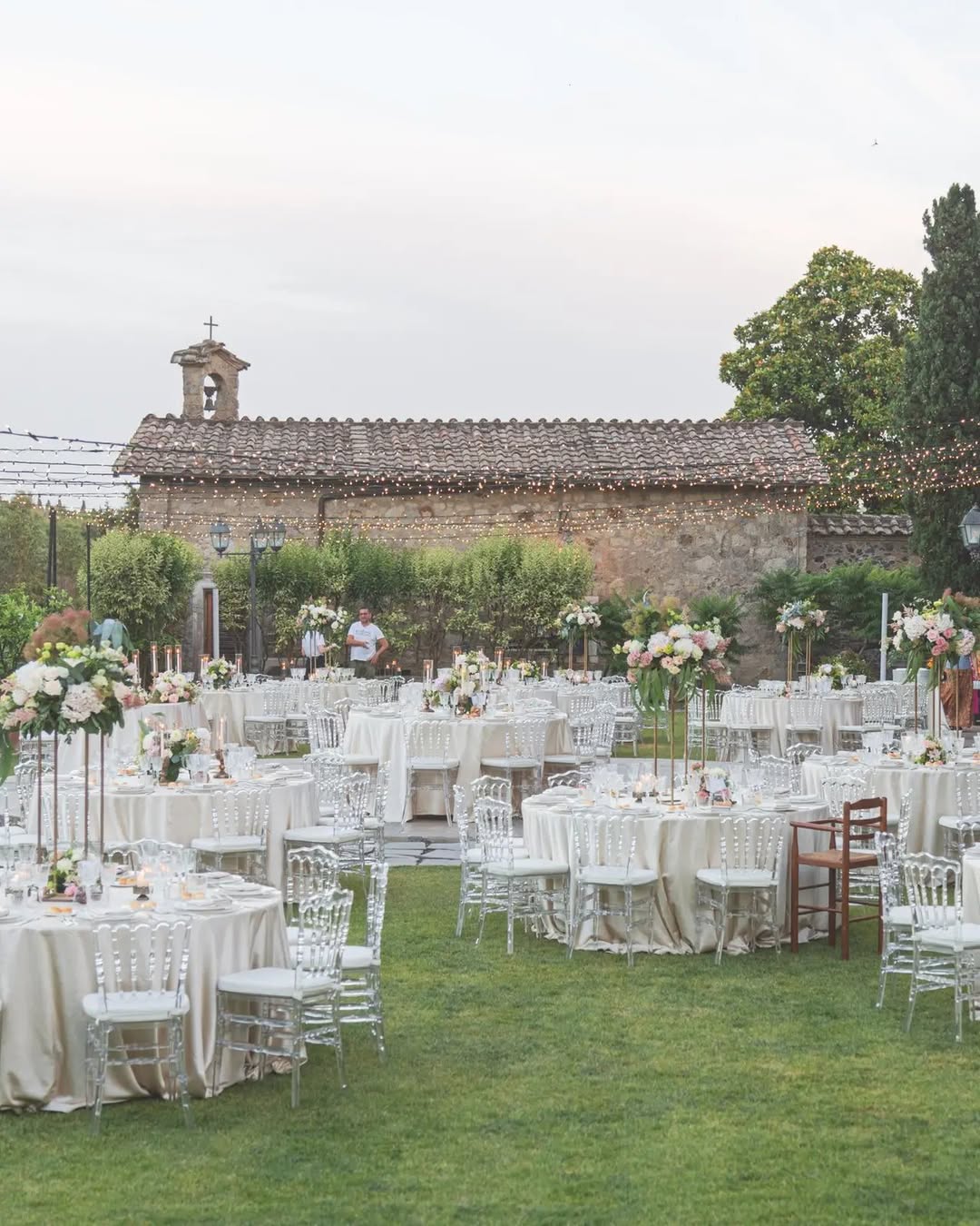 Outdoor wedding reception setup at Castello della Castelluccia with round tables, neutral linens, and floral centerpieces under string lights, a top choice among Rome wedding venues.